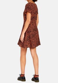 Robe courte à manches courtes, coupe évasée, de couleur rouille avec un motif animalier noir. Fabriquée en tissu léger, elle présente une finition texturée.