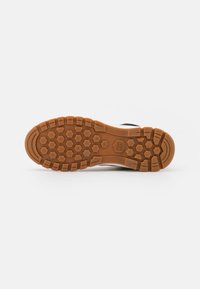 Brown rubber outsole with a hexagonal pattern, featuring grooves for traction and stability. Smooth edges with a clear brand logo.