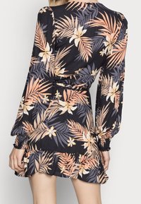 Vestido envolvente floral con mangas largas, que presenta una mezcla de flores melocotón y blancas sobre un fondo negro, tejido texturizado y dobladillo con volantes.