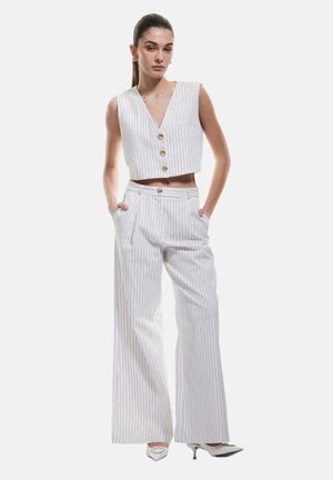 Top corto bianco a righe con scollo a V e tre bottoni, abbinato a pantaloni a gamba larga con tasche laterali e un bottone coordinato in vita.