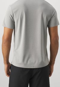Camiseta gris de manga corta con textura suave y cuello redondo, presenta un ligero estiramiento y un ajuste regular. Vista trasera mostrada.