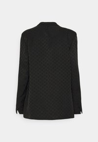 Blazer noir texturé à manches longues avec col cranté, montré de dos sur un fond clair uni.