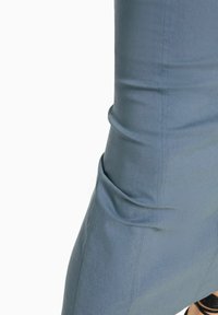 Jasnoniebieskie dopasowane spodnie o gładkiej fakturze, z bocznymi kieszeniami i detalami szwów, zwężające się ku kostce.