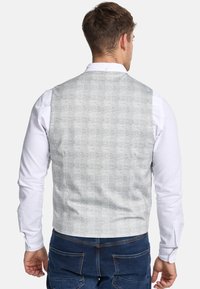 Graue Weste mit strukturiertem Muster und glatter Oberfläche. Wird über einem weißen Langarmhemd getragen, Ansicht von hinten.