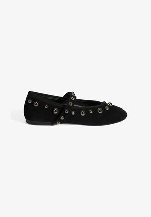 Ballerines en suède noir avec un bout rond, une bride à la cheville et des accents décoratifs en métal noir le long des côtés.