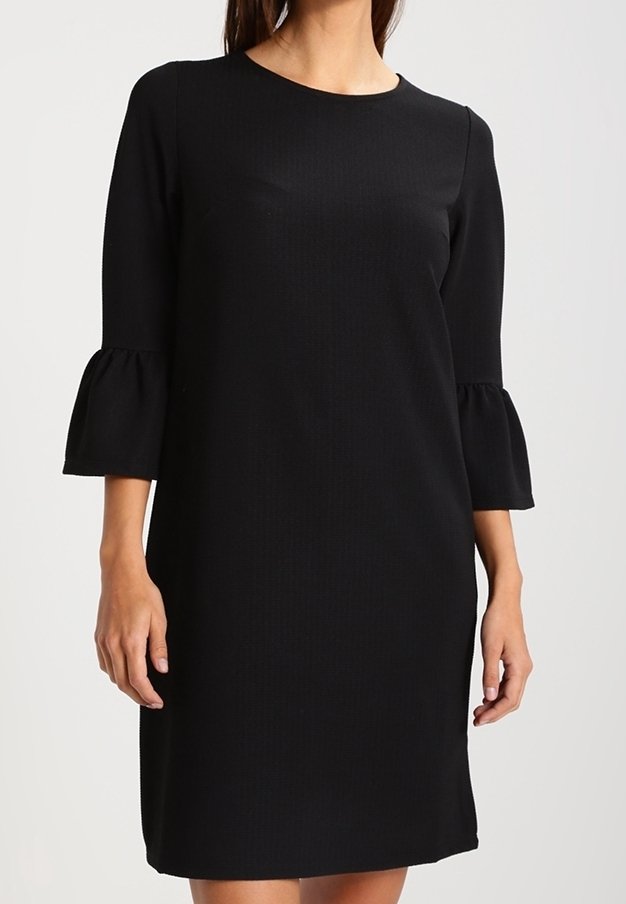 Svart klänning med rund halsringning och trekvartsärmar som har volangdetaljer. Slät tyg med en något strukturerad mönster.