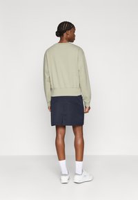 Sweatshirt verde claro com bainha canelada, combinado com uma saia azul-marinho com bolsos traseiros e uma pequena fenda. Ténis brancos e meias até ao tornozelo.
