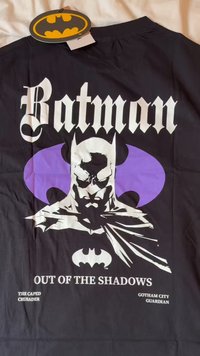 Camiseta negra con un diseño gráfico de Batman con acentos morados. El texto dice "Batman" y "Fuera de las Sombras" en letras blancas en negrita.