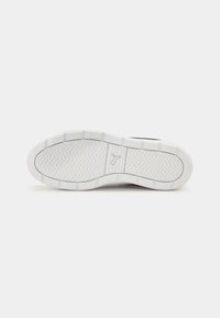 Sole di sneaker bianca con una superficie texture, caratterizzata da un motivo a zigzag. Forma curvata con un logo prominente al centro.