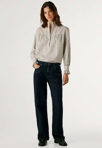 Blusa de cuadros clara con cuello alto y detalle de volantes, combinada con pantalones vaqueros de pierna ancha azul oscuro. Unos zapatos negros completan el conjunto.