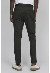 Pantalones ajustados de color verde oscuro con una textura suave, que cuentan con dos bolsillos traseros y se combinan con zapatillas blancas.