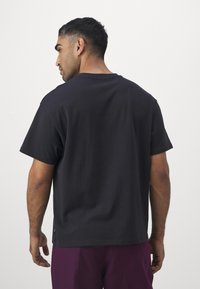 Zwarte katoenen t-shirt met korte mouwen, relaxte pasvorm en een ronde halslijn; heeft een klein logodetail nabij de zoom.