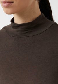 Brauner, figurbetonter Rollkragenpullover aus weichem Stoff mit glatter Textur; verfügt über einen hohen Ausschnitt und minimale Nahtdetails.