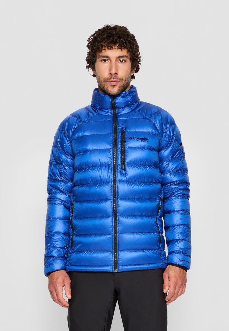 Veste doudoune isolée bleue avec un col montant, fermeture éclair sur le devant et poignets élastiques. Présente une poche poitrine et une texture brillante et matelassée.