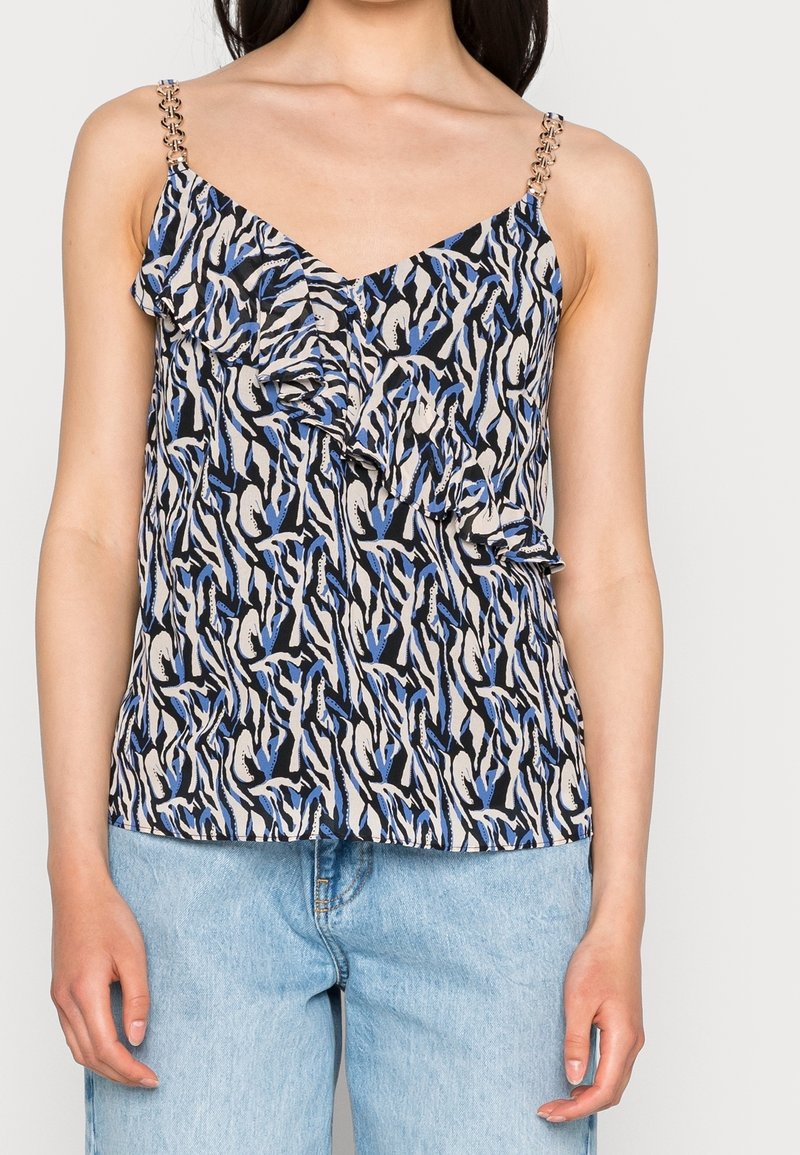 Camisole à motif floral en noir, blanc et bleu avec un détail volanté sur le devant et des bretelles en maillons de chaîne. Associée à un denim bleu clair.