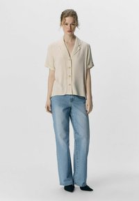 Ljust beige kortärmad skjorta med knappframside-design. Kombinerad med högmidjade, raka ljusblå jeans och spetsiga svarta skor.