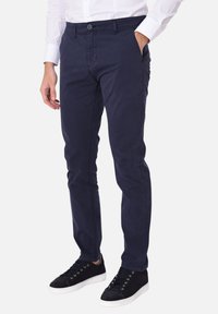 Pantaloni in cotone blu navy con vestibilità slim, dotati di cinque tasche, chiusura a bottone e una texture liscia. Abbinati a sneaker nere.