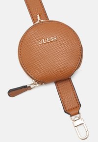 Brązowy okrągły portfel na monety o teksturowanej powierzchni z zamkiem błyskawicznym, przymocowany do pasującego paska z zapięciem w kolorze złotym oraz logo GUESS z przodu.