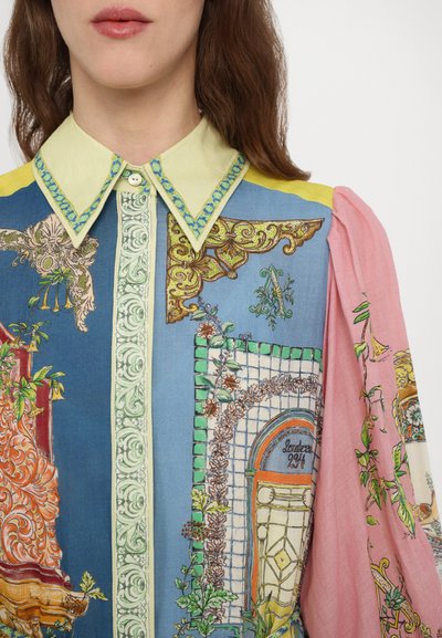 Multicolored shirt features a yellow and blue design with floral and architectural prints, a green button placket, and pink puff sleeves.