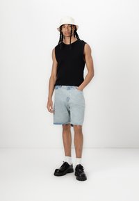 Black sleeveless knit top, light blue denim shorts, black chunky shoes, and a white bucket hat. Smooth textures and relaxed fit.