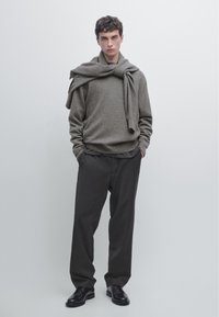 Un pull en tricot gris porté sur une chemise gris foncé, associé à un pantalon large sombre et des chaussures noires. Design simple et minimaliste avec une coupe décontractée.