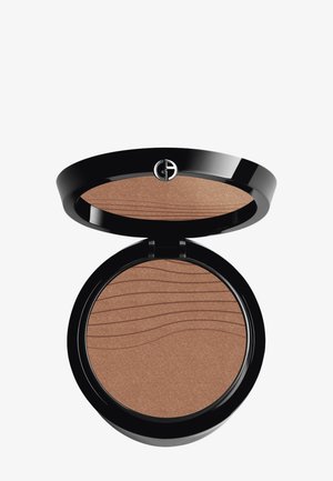 Bronzer i en svart, sirkulær kompakt med en jevn, varm brun pulveroverflate som har bølgemønstre. Åpnes med et elegant hengsel.