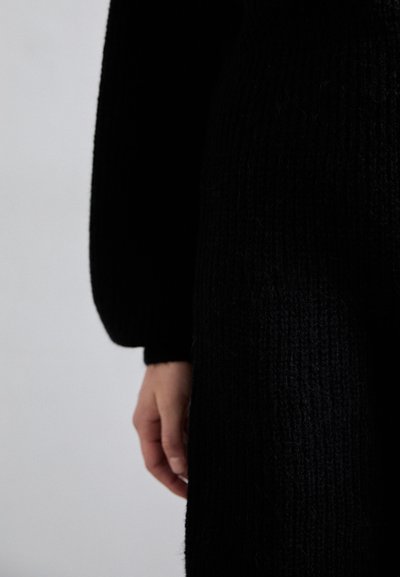 Pulover negru tricotat cu un model texturat, având mâneci lungi și un design ajustat, expus pe un fundal deschis.