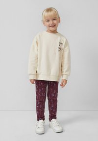 Kremowy sweatshirt z napisem "MIŁEGO DNIA" na piersi, w połączeniu z bordowymi legginsami w kwiaty i białymi sneakerami.