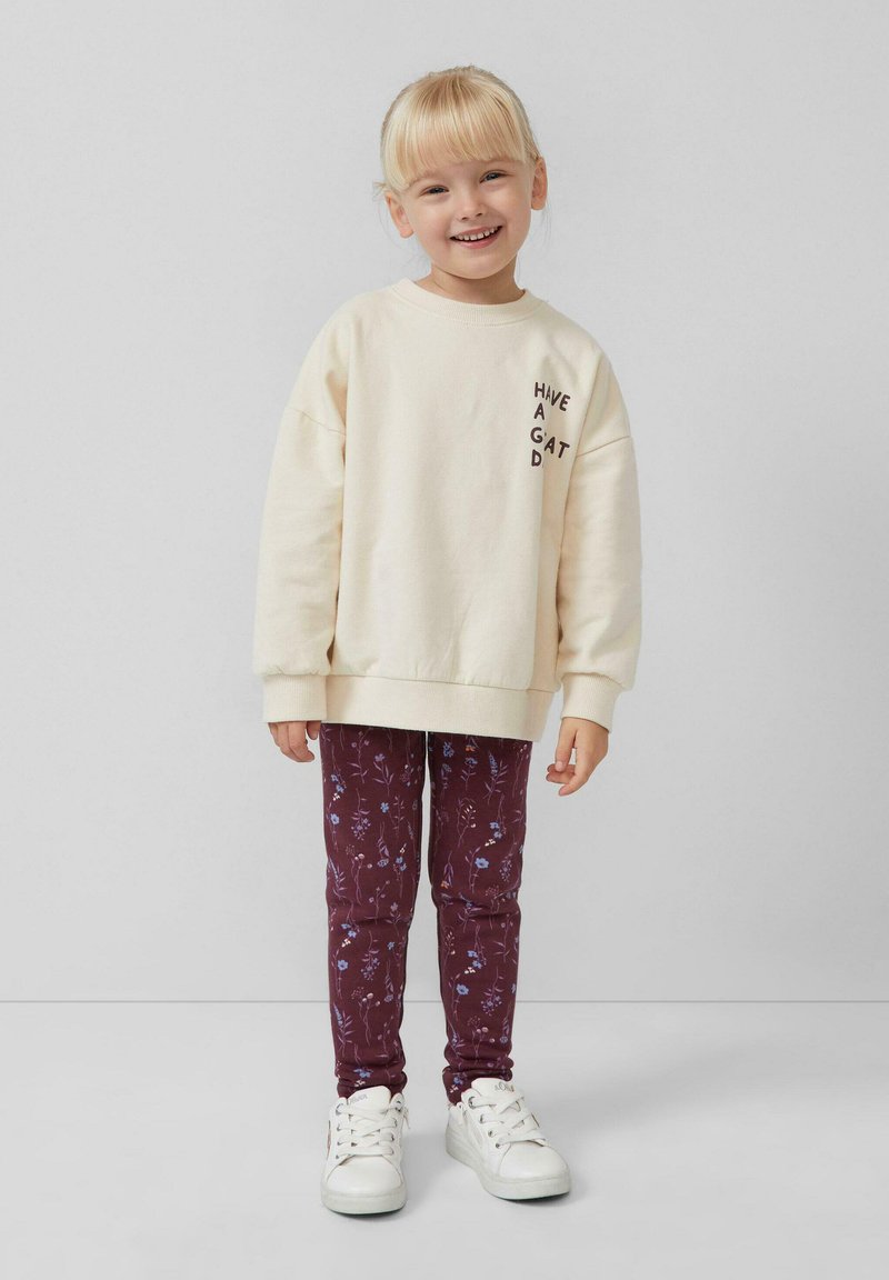 Kremowy sweatshirt z napisem "MIŁEGO DNIA" na piersi, w połączeniu z bordowymi legginsami w kwiaty i białymi sneakerami.