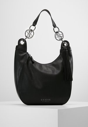 Schwarze Guess Lederschultertasche mit silbernen Logoakzenten, Quasten-Detail und einem einzelnen Griff auf weißer Oberfläche.