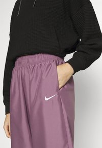 Svart texturerad hoodie med en avslappnad passform, i kombination med ljuslila joggers med elastisk midja och en vit Nike-logotyp på framsidan.