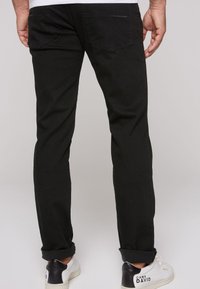 Jeans in denim nero con una vestibilità dritta, cuciture a contrasto e due tasche posteriori. Abbinati a scarpe da ginnastica bianche con accenti neri.