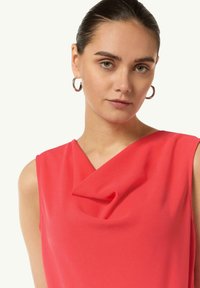Czerwona bluzka bez rękawów z dekoltem w kształcie drapowania. Wykonana z miękkiego materiału, charakteryzująca się gładką fakturą i prostym, eleganckim wzornictwem.