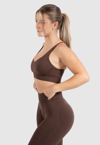 Sostén deportivo marrón con diseño de escote en V y tirantes anchos, combinado con leggings de cintura alta que presentan acentos texturizados y una construcción sin costuras.