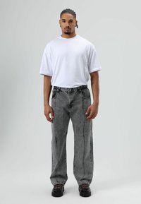 Witte oversized t-shirt, vervaagde zwarte jeans met zijstiksels en zwarte plateauzolen met rode veters. Minimalistisch ontwerp, casual pasvorm.