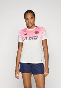 White sports jersey with pink gradient shoulder, red logo, and navy shorts. Material is lightweight, with a smooth texture and breathable design.