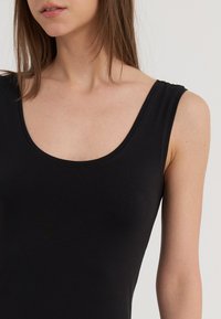 Svart ärmlös topp med vid rundad halsringning, tillverkad av ett smidigt, stretchigt material, figurnära design som framhäver nyckelben och axlar.