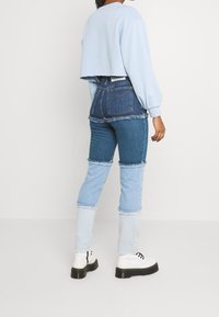 Sudadera corta de color azul claro, combinada con jeans de mezclilla de patchwork que presentan varios tonos de azul, con dobladillos deshilachados y zapatos de plataforma negra gruesa.
