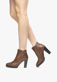Brown leather ankle boots with a high block heel, zip closure, and decorative studs on the collar. Smooth texture with a sleek design.
