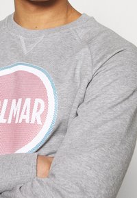 Felpa grigia con un design grafico rotondo che presenta "ALMAR" in testo bianco, uno sfondo rosso con accenti blu e un tessuto testurizzato.