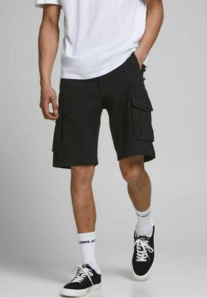 Pantaloni cargo neri con molte tasche laterali, vestibilità regolare, tessuto testurizzato, abbinati a calze bianche e sneakers nere.