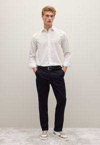 Wit gestreept shirt met een knoopsluiting, donkerblauwe broek, gevlochten zwarte riem en beige sneakers. Vlakke, gladde texturen en een ontspannen pasvorm.