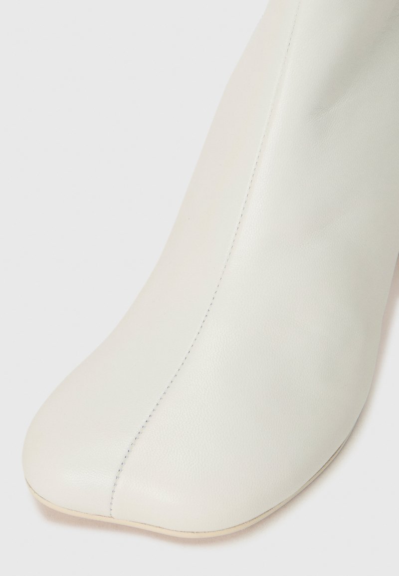 Stivale alla caviglia in pelle bianca con punta affusolata, texture liscia e dettagli di cucitura discreti lungo il lato. Tacco basso e sottile.