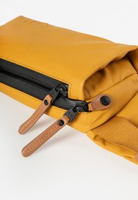 Gele waterdichte tas met een textuur oppervlak, uitgerust met dubbele zwarte ritsen, tan leren trekkoorden en een contrasterende stofaccent.