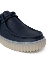 Scarpa in pelle blu con punta arrotondata, dotata di un dettaglio cucito bianco e una suola trasparente scanalata per una maggiore aderenza.