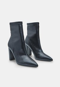 Botines de cuero negro con punta afilada y tacón cuadrado, con un diseño sin costuras y costuras en contraste a lo largo de los bordes.