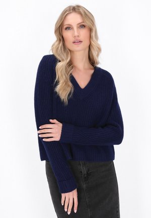 Marineblauwe gebreide trui met een V-hals, geribde textuur en lange mouwen. Draagt een zwarte rok, met een losse pasvorm en een verkorte lengte.