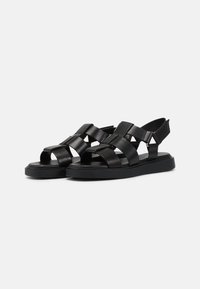 Sorte sandaler med brede kryssremmer, flat såle og bakrem. Laget av glatt lær med matthinne og minimalistisk design.
