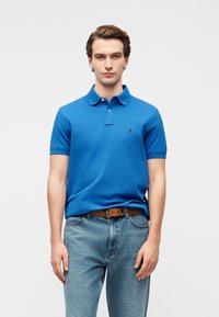 Polo bleu en coton avec col et manches courtes. Il présente un petit logo sur la poitrine, associé à un jean bleu clair.