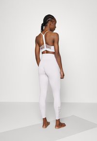 Top desportivo branco com um design em corte listrado na parte de trás, combinado com leggings brancas de cintura alta com detalhe de atacadores nas bainhas.